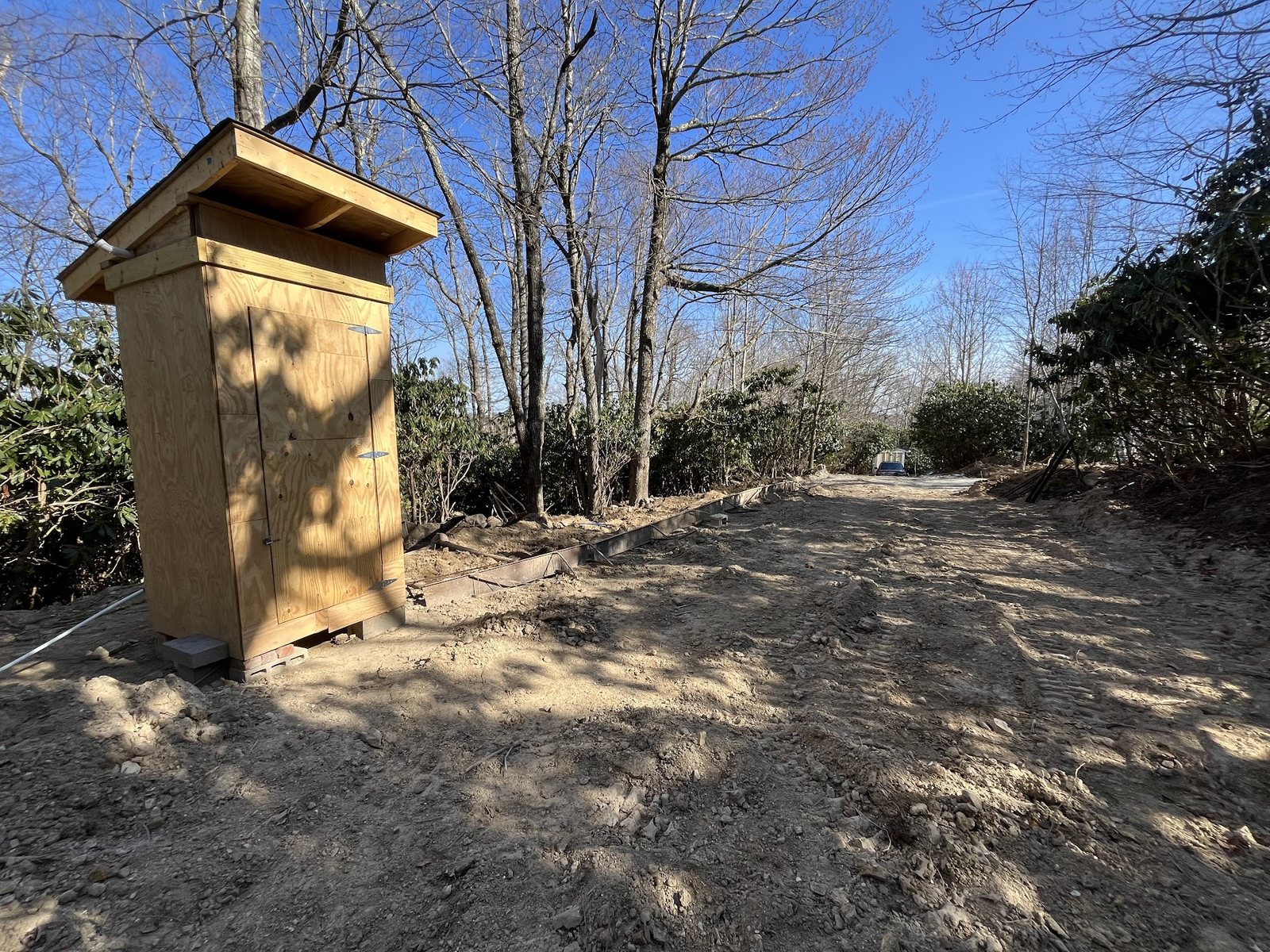 Finished graded dirt access road on a sunny day, with a built plywood utility structure alongside