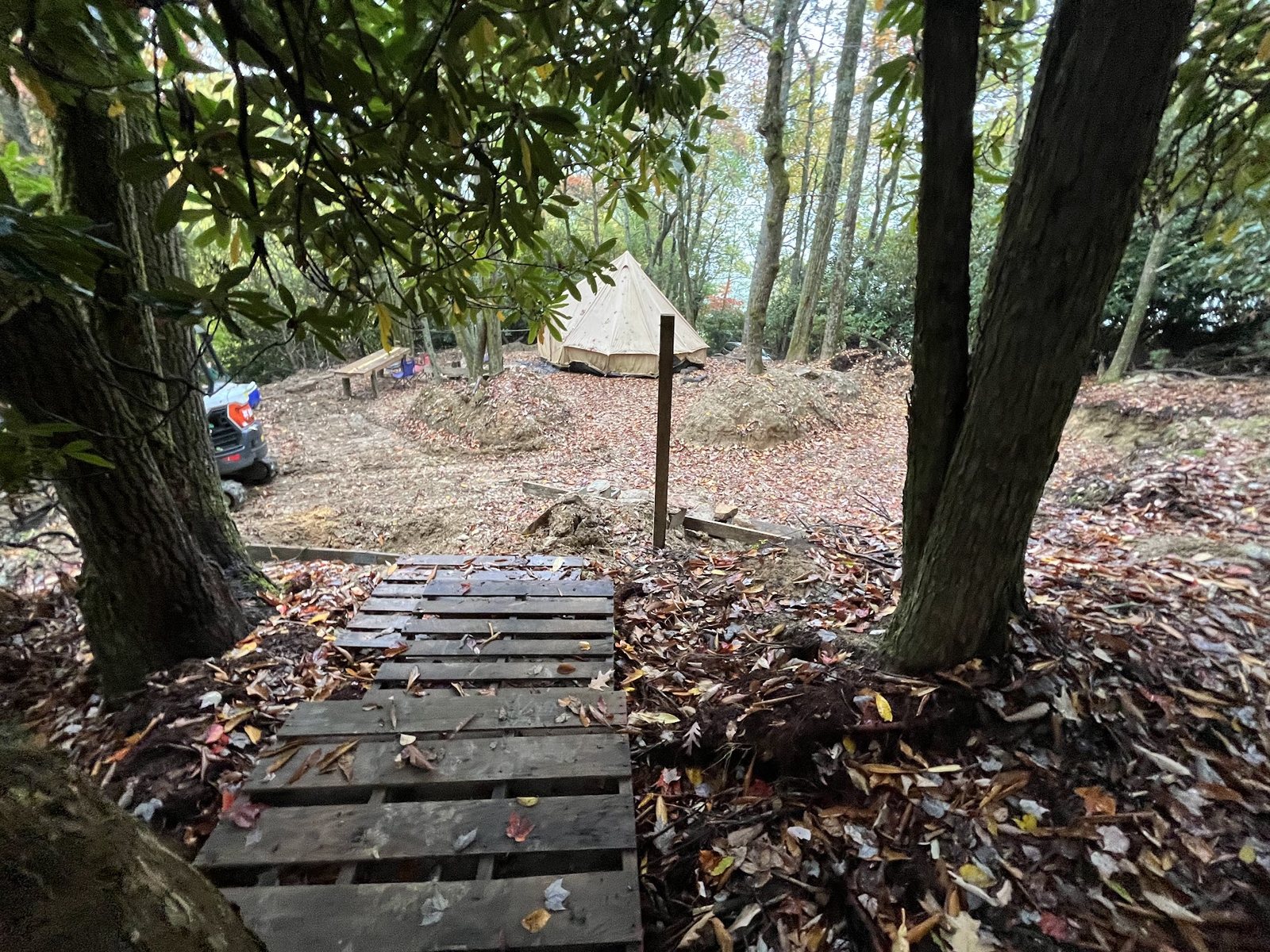 Reclaimed pallet-board steps leading down through the trees to a cleared camp bench with tent, cooler, and bench seating