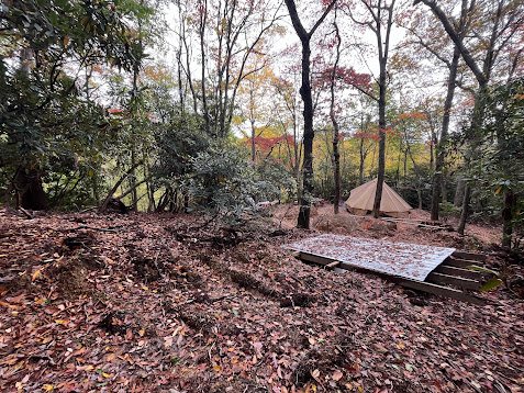 Graded camp bench with drainage swales cut into the dirt, wall tent visible in the background