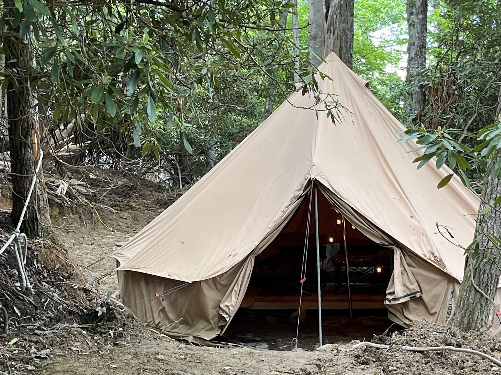 Finished canvas wall tent set up on a wood platform among trees, lit from inside