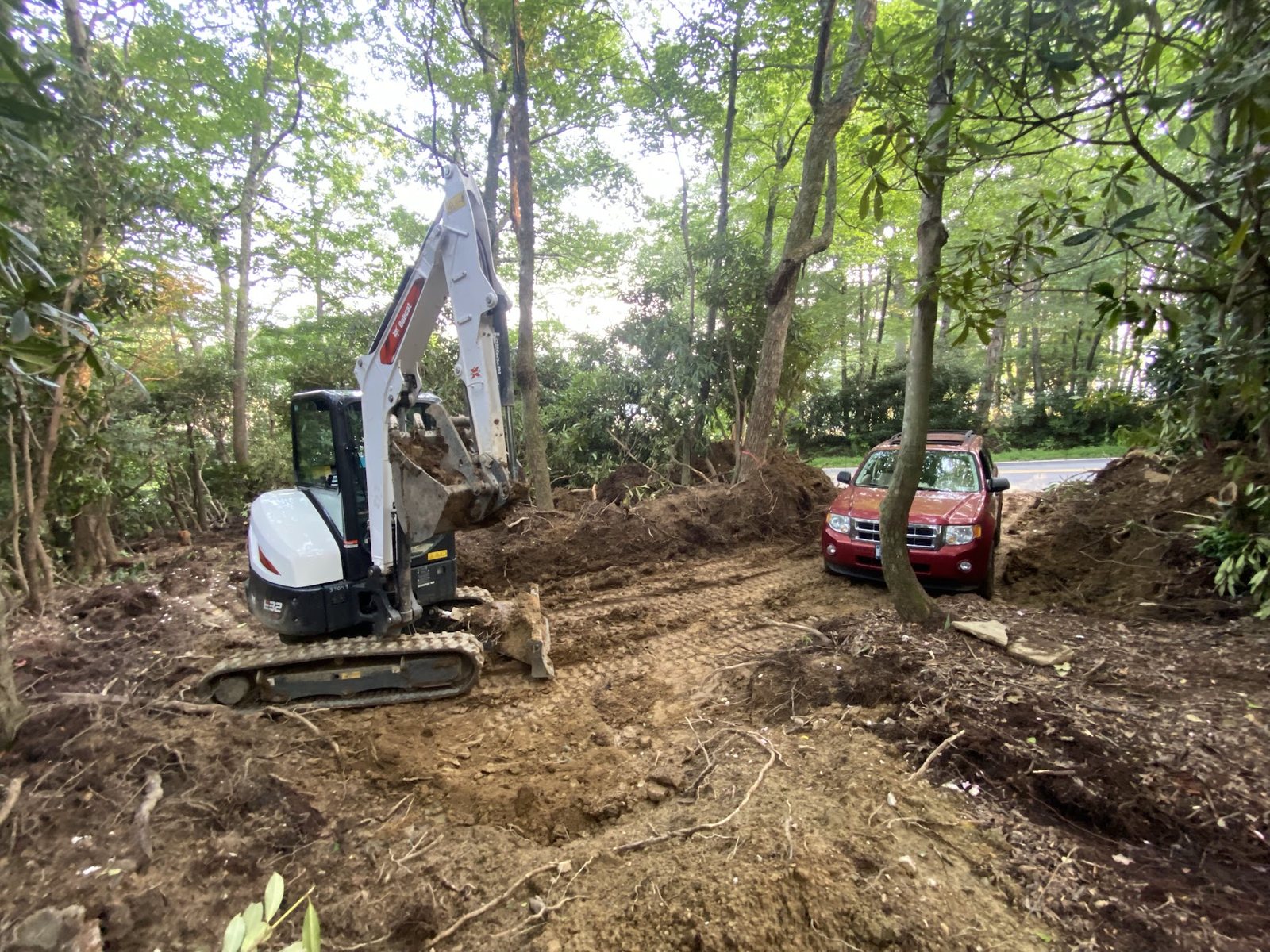Bobcat E32 grading a flat pad after clearing, a red SUV parked on the newly graded surface